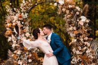 16 a boho lux fall wedding arch decorated with blush, rust-colored, peachy blooms, fronds, grasses, leaves and a baby’s breath