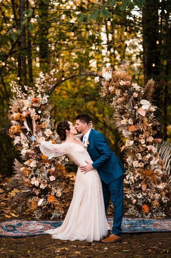 a boho lux fall wedding arch decorated with blush, rust-colored, peachy blooms, fronds, grasses, leaves and a baby's breath