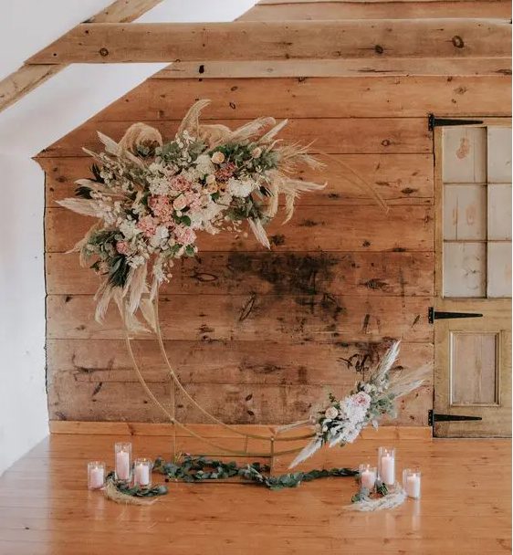 a boho celestial wedding altar of a metal half moon, white and blush blooms, greenery and pampas grass and pillar candles