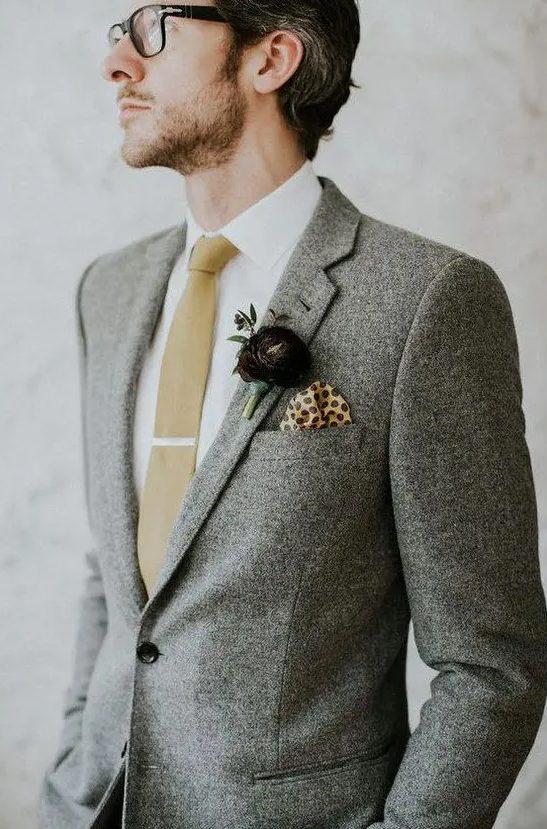 a grey tweed suit, a white button down, a tan tie, a dark purple floral boutonniere for an elegant winter groom's look
