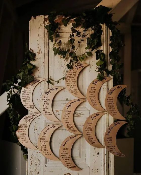 a moon shaped seating chart decorated with greenery is a cool idea for a celestial wedding