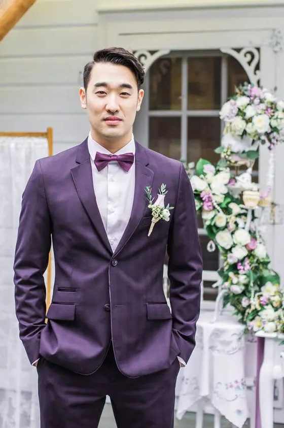 a bright groom's look with a purple plaid suit, a white shirt, a purple bow tie and a blush boutonniere