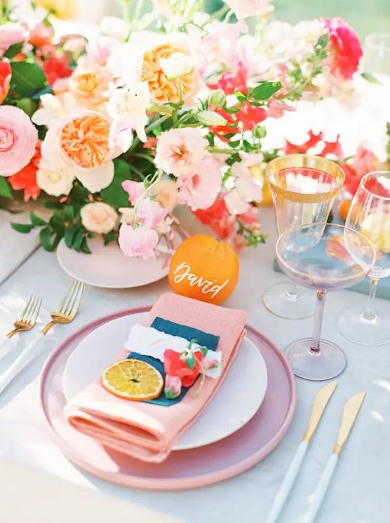 a bold and cheerful summer wedding tablescape with bright blooms, pink plates and napkins, gold rim glasses and cutlery