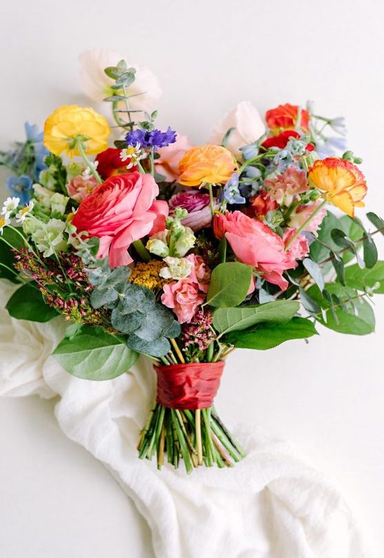 a bright summer wedding bouquet with pink, yellow, purple and blue flowers and greenery for a refined summer wedding