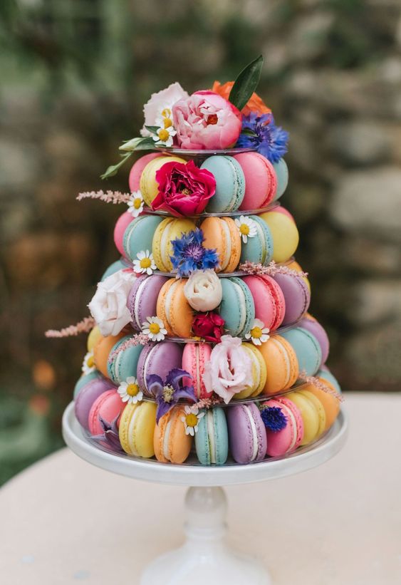 a colorful macaron tower decorated with bold blooms and leaves is a fantastic alternative to a wedding cake