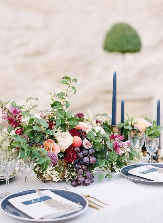 a beautiful centerpiece with blush and burgundy blooms, leaves and grapes in a gold bowl