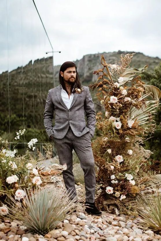 a stylish boho groom's look with a grey checked suit, a white shirt and a dried flower boutonniere is cool
