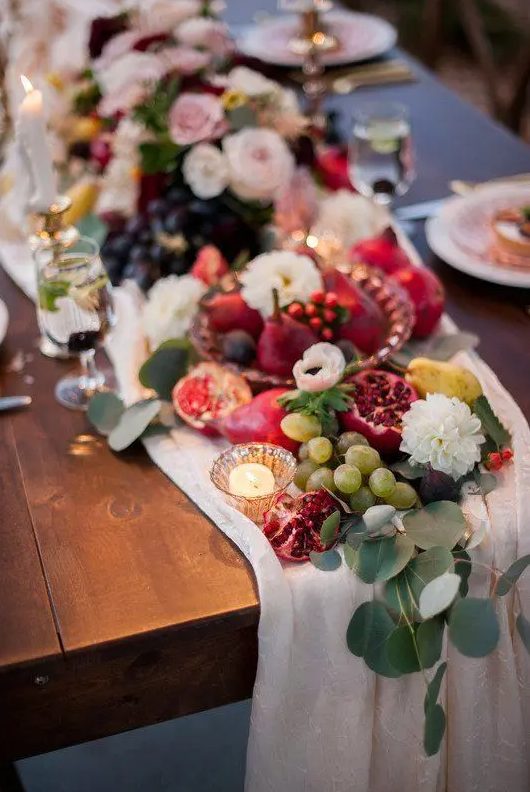 a super lush wedding table runner with white blooms, grapes, pears and eucalyptus, candles and a white fabric runner for a fall wedding