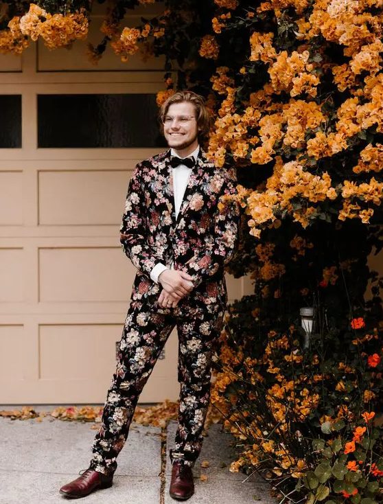 a moody floral suit, a white shirt, a black bow tie and brown shoes is a bold option for a fall wedding