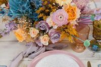 52 a bright wedding tablescape with an iridescent wedding floral arrangement, a pink charger, gold cutlery and colored glasses for an iridescent wedding
