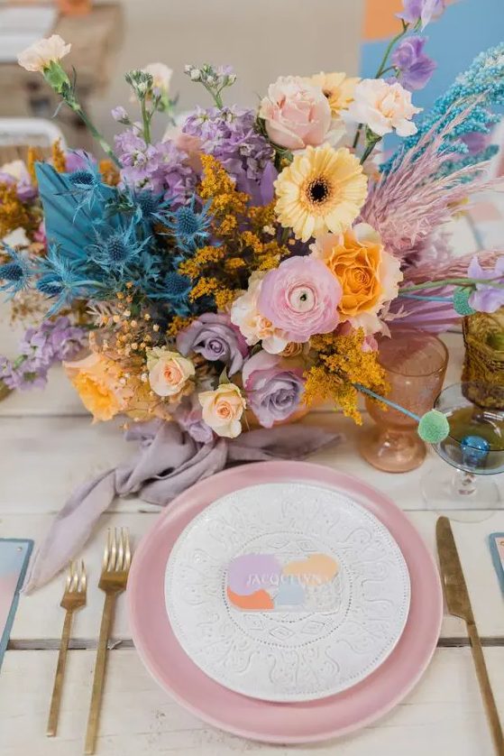 a bright wedding tablescape with an iridescent wedding floral arrangement, a pink charger, gold cutlery and colored glasses for an iridescent wedding