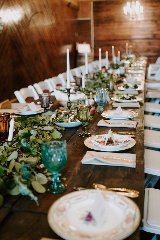 a pretty neutral wedding tablescape with patterned plates, candles, greenery, green and grey glasses