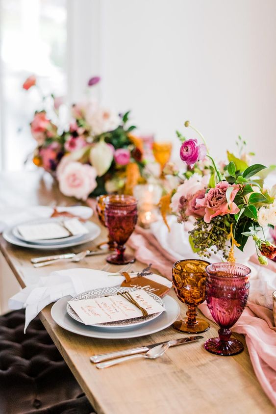 a bright and catchy wedding tablescape with pink and blush blooms, greenery, grey plates and pink and amber glassware