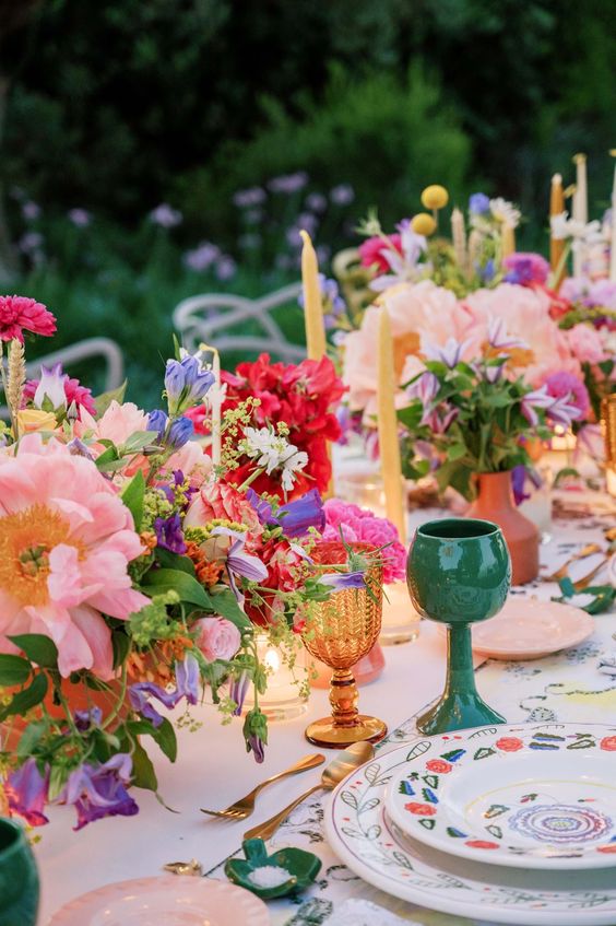 a colorful wedding table setting with printed plates, bright blooms and greenery and amber and green glasses