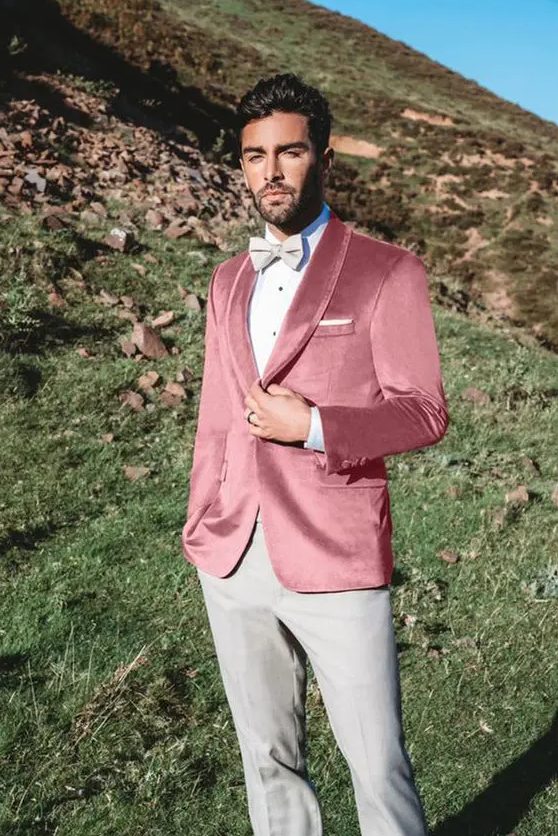 a refined groom's look with grey trousers and a bow tie, a pink velvet blazer, a white shirt with black buttons