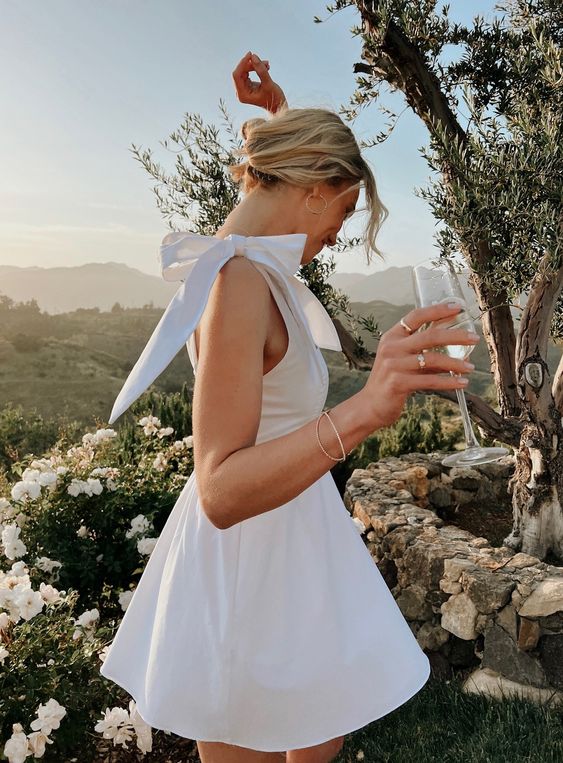 a white mini bridesmaid dress with a bow on the shoulder is a cool and catchy idea for a modern wedding