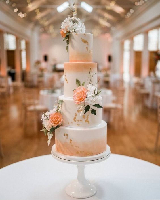 a Peach Fuzz wedding cake with watercolors, white and peachy blooms and greenery plus gold leaf for more elegance