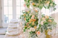 a beautiful peach and cream wedding tablescape with blush glasses, peachy, blush and white blooms and greenery decorating the table in a lush way