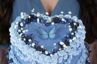 a blue heart-shaped lambeth wedding cake topped with blooms, berries and a single blue butterfly is a cool idea