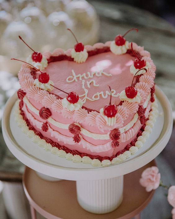 a bold pink heart-shaped wedding cake with pink and white sugar detailing and calligraphy plus cherries on top