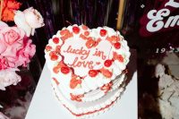 a bright heart-shaped wedding cake decorated with calligraphy and red blooms and bows is a cool and catchy wedding dessert