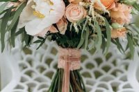a chic wedding bouquet with peachy, pink and white blooms and greenery plus pink lace wrap and ribbons