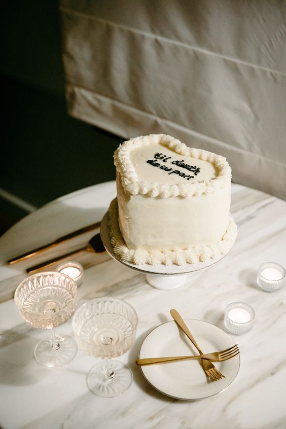 a classic white buttecream heart-shaped wedding cake with some detailing and black calligraphy is a cool idea