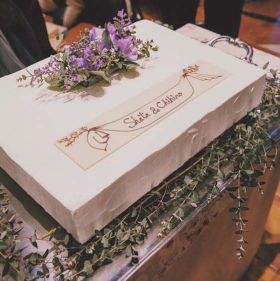 a classy white sheet wedding cake topped with fresh blooms and greenery and with calligraphy is a cool and catchy idea for a wedding