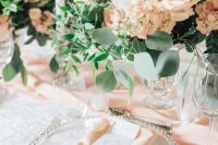 a delicate peach and cream wedding table setting with peachy and white blooms, peachy linens, white candles and greenery