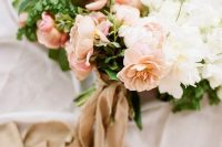 a delicate wedding bouquet with peachy and white blooms and greenery and tan colored ribbons is a beautiful idea