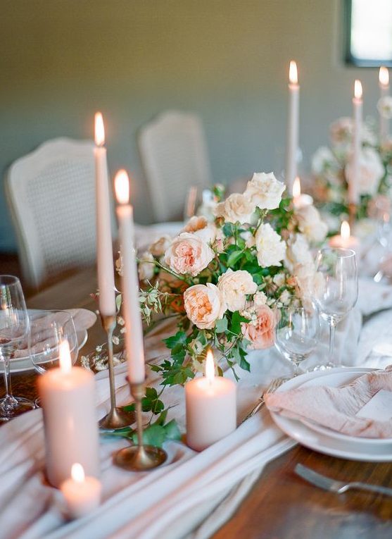 a dreamy wedding tablescape with a blush runner, peachy candles and napkins, greenery and white porcelain is chic
