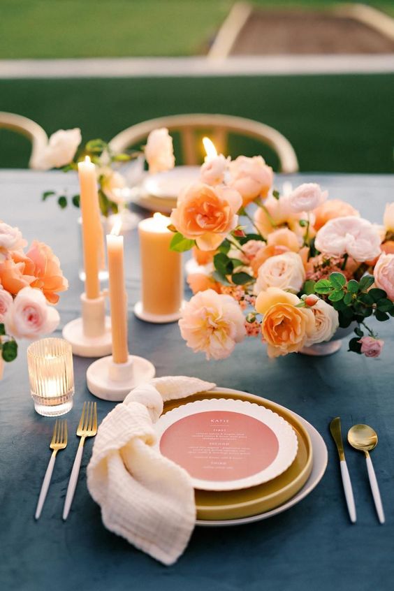 a modern wedding tablescape with a blush and peachy floral centerpiece, mustard and white plates, peachy candles