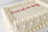 a neutral kitschy wedding cake with icing and red calliphy is a cool and fun idea for a wedding