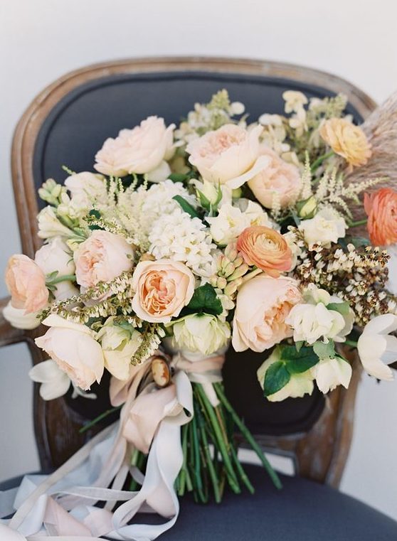 a peachy and creamy wedding bouquet with various blooms, greenery and even pampas grass plus white ribbons