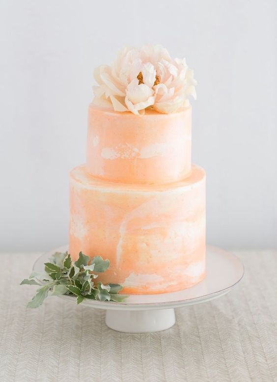a peachy watercolor wedding cake with a blush bloom on top and some greenery is amazing for spring or summer