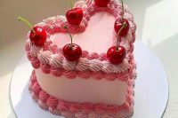 a pink heart-shaped wedding cake with sugar detailing and cherries on top is a colorful and catchy dessert to rock