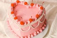 a pink heart-shaped wedding cake with sugar details and cherries on top is a cool vintage-inspired idea for a wedding