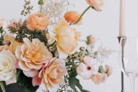 a pretty peachy and creamy plus blush floral wedding centerpiece with greenery and white candles in vintage candleholders