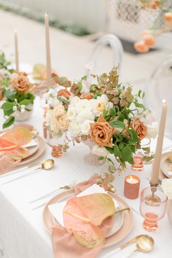 a pretty summer wedding tablescape with a lovely white, peachy and blush centerpiece, blush plates and peachy blooms and candles