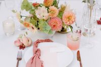 a pretty wedding tablescape accented with a pink napkin and peachy and pink blooms and greenery