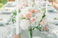 a pretty wedding tablescape with peachy, blush and white blooms, peachy candleholders and white candles for summer