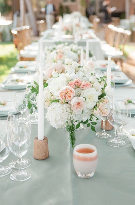 a pretty wedding tablescape with peachy, blush and white blooms, peachy candleholders and white candles for summer