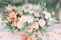 a refined peachy wedding tablescape with peachy, pink and rust blooms and greenery, a peachy table runner and glasses plus gold cutlery