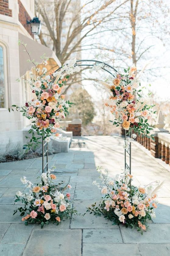 a refined wedding arch with blush, orange, peachy and mauve blooms, greenery and white blooming branches is chic