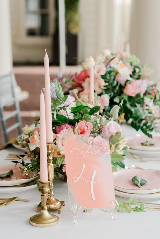 a refined wedding tablescape with peachy plates, candles and a table number and beautiful peachy and coral blooms with greenery