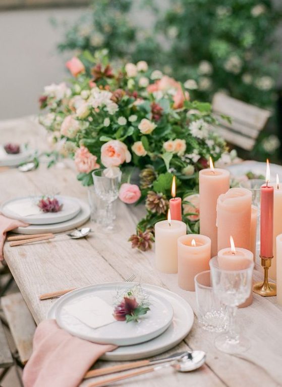 a romantic wedding tablescape with peachy candles and napkins, peachy and orange blooms, greenery and cutlery with peachy handles