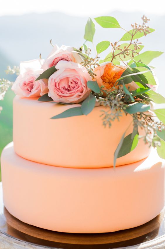 a sleek and plain peach wedding cake with peach and pink blooms and greenery is amazing for a summer wedding