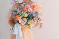 a spring bride rocking a sheer peachy wedding dress and a bold bouquet looks adorable