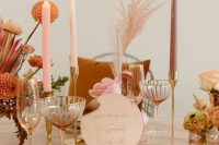 a sunset-colored wedding tablescape with dusty pink, blush and peachy elements, candles and gold cutlery
