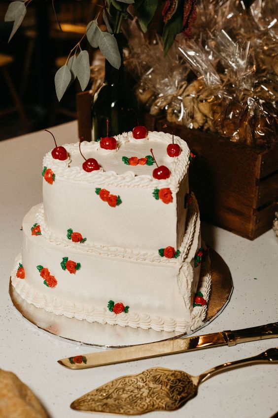 a white heart-shaped wedding cake decorated with small sugar blooms and cherries on top is a cool idea